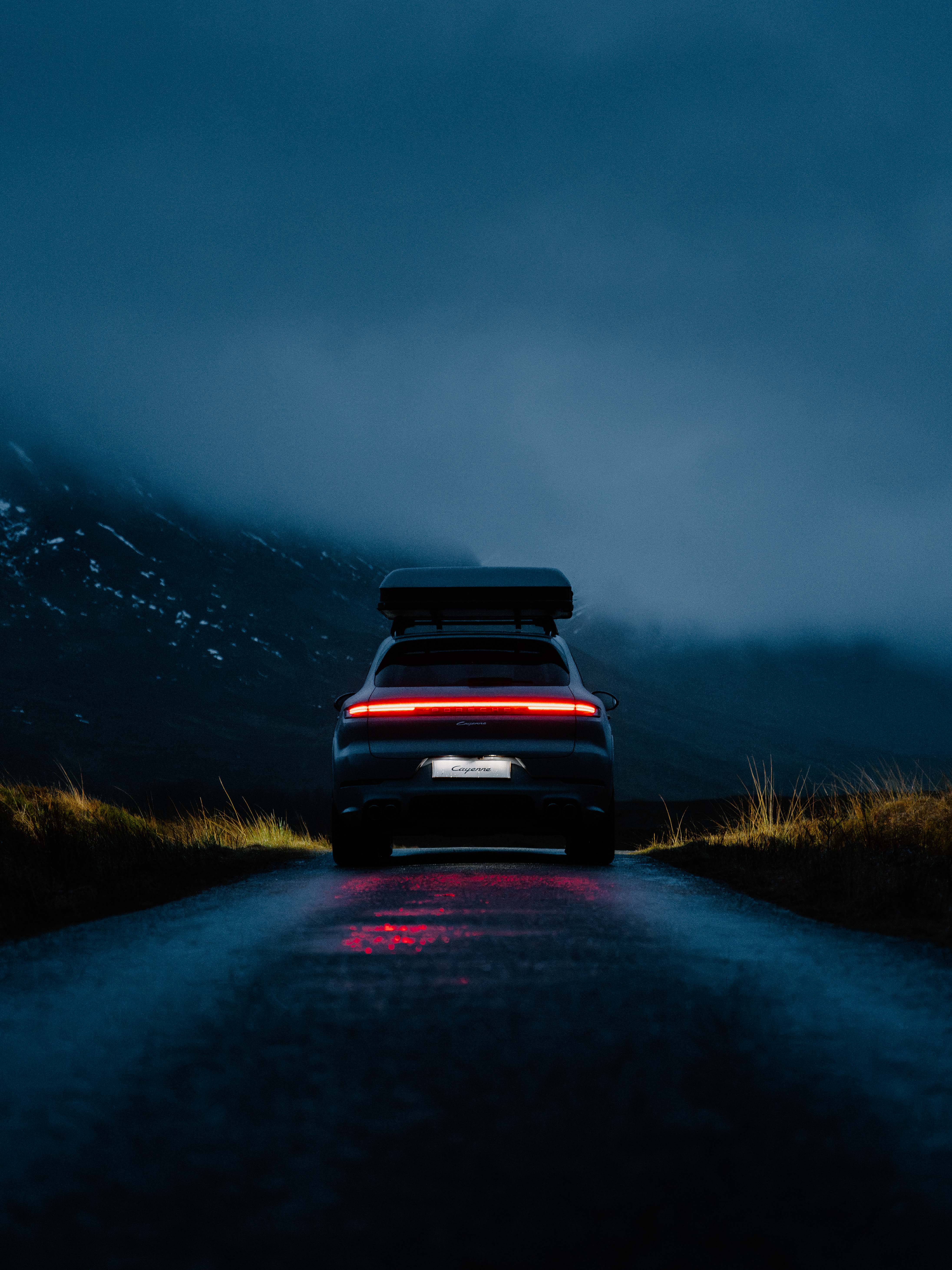 The back of a Porsche driving through a foggy landscape at dusk